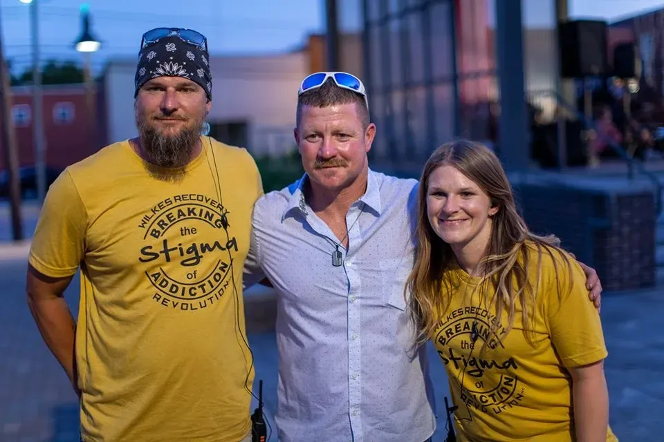 A person in blue gloves examines a medication guide next to vials, syringes, and a bowl of medication caps on a table